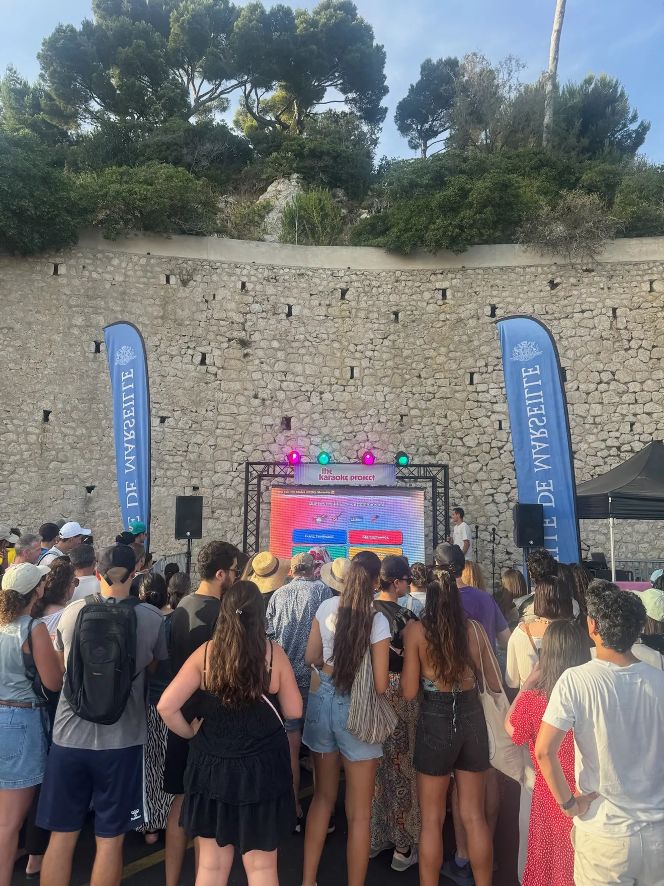 Le public joue au blind test devant l’écran, entre les drapeaux de la Ville de Marseille