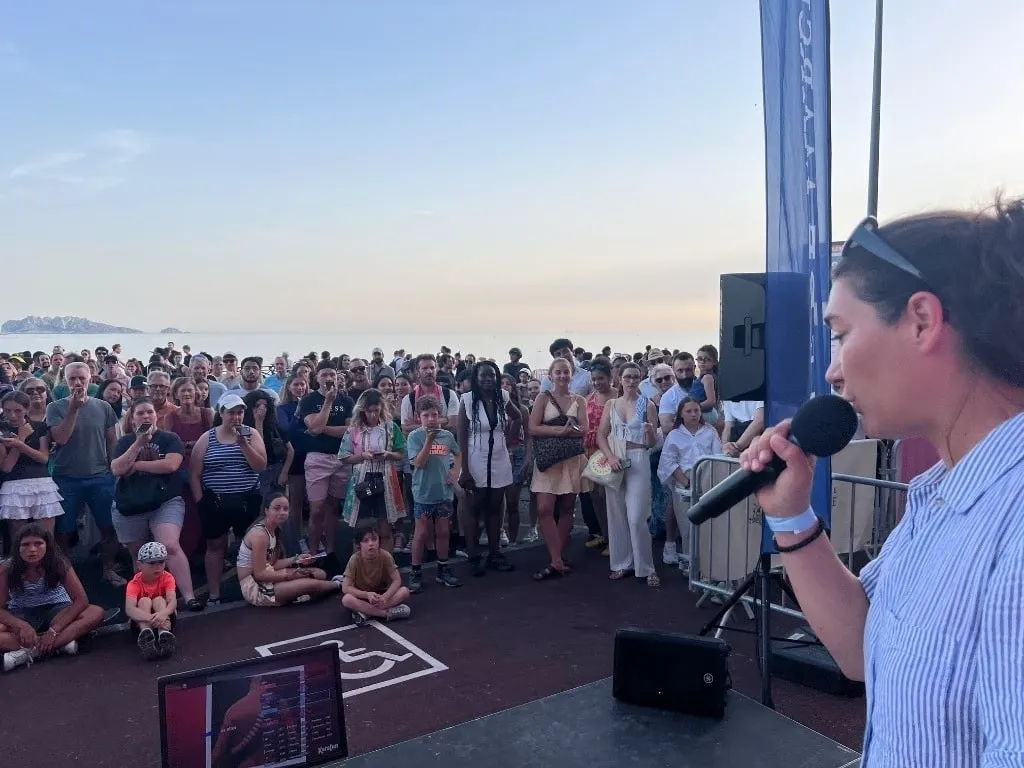 L’animatrice face au public massé devant la scène, la mer en arrière-plan