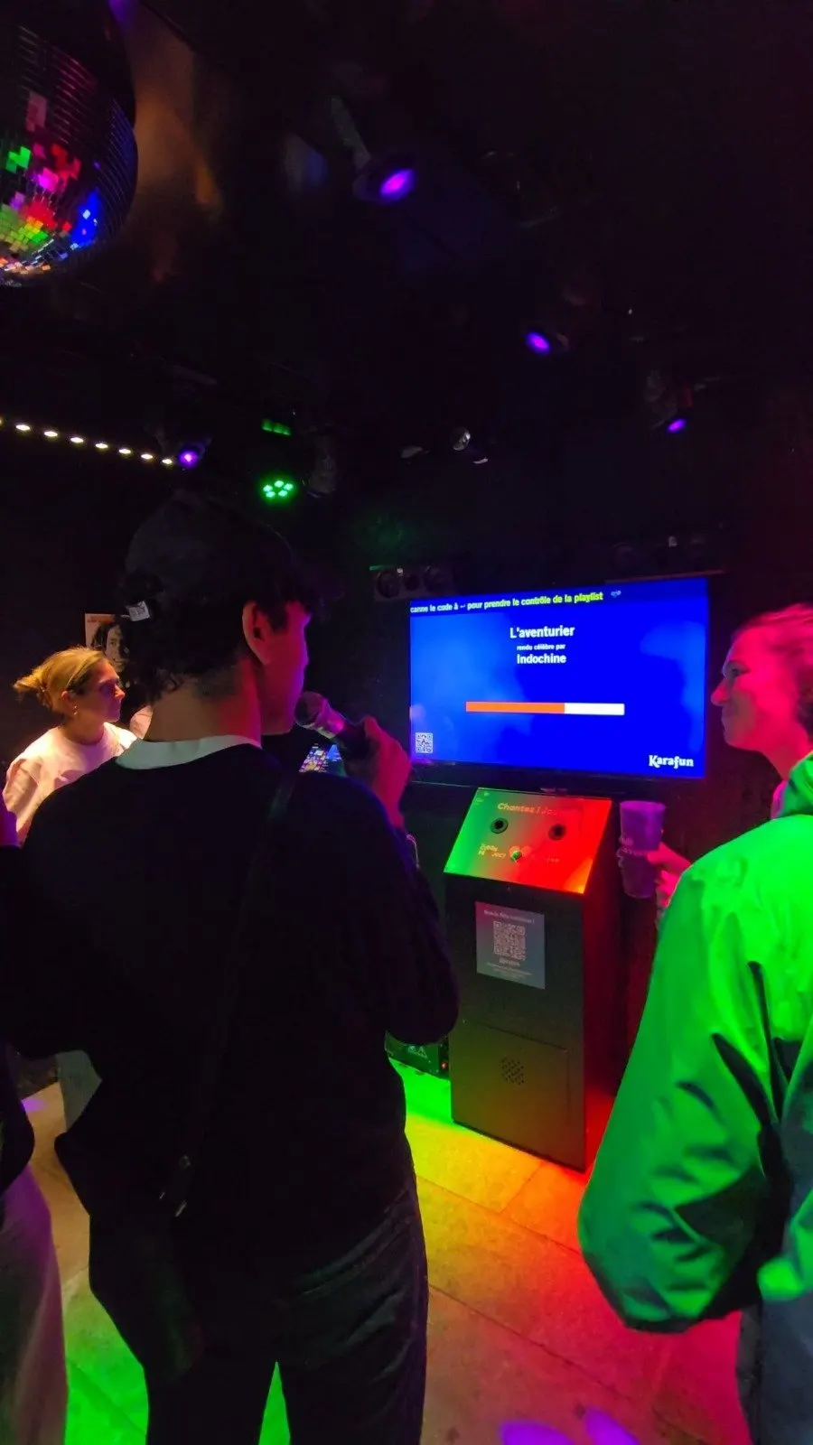 L’intérieur de la box karaoké : écran, borne et micros, lumières de soirée